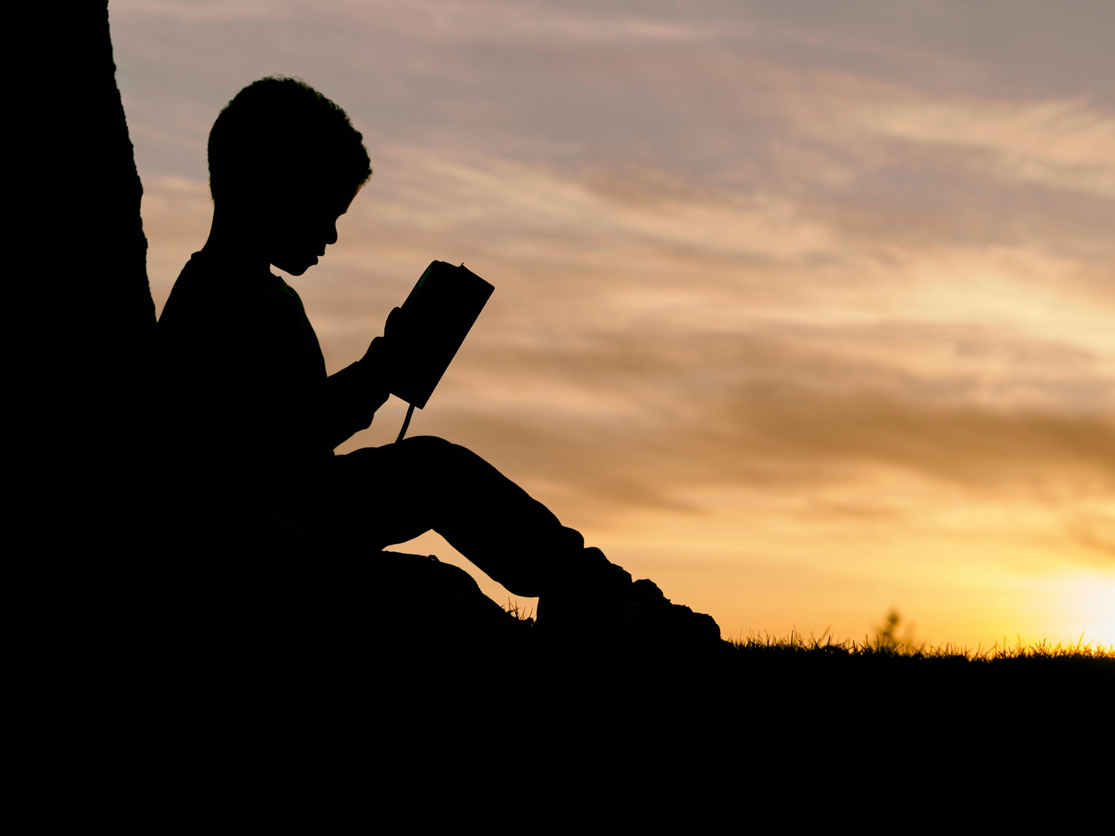 Silhouette of child sitting by a tree and reading