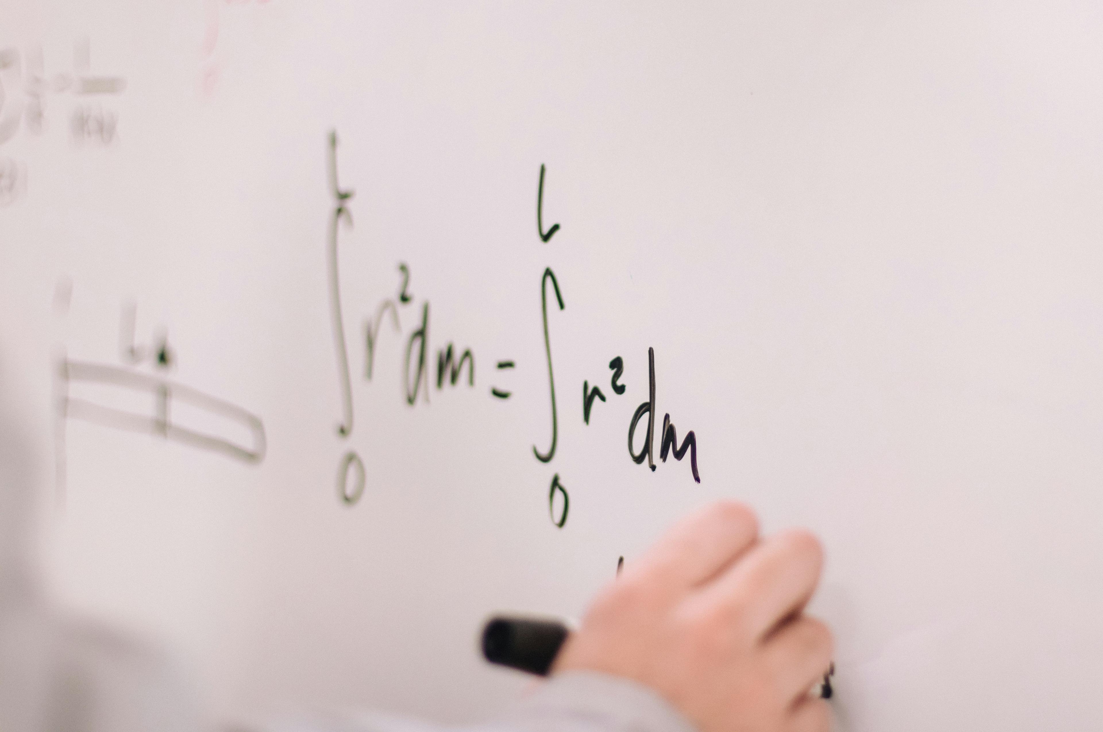 Math equations being written on a whiteboard